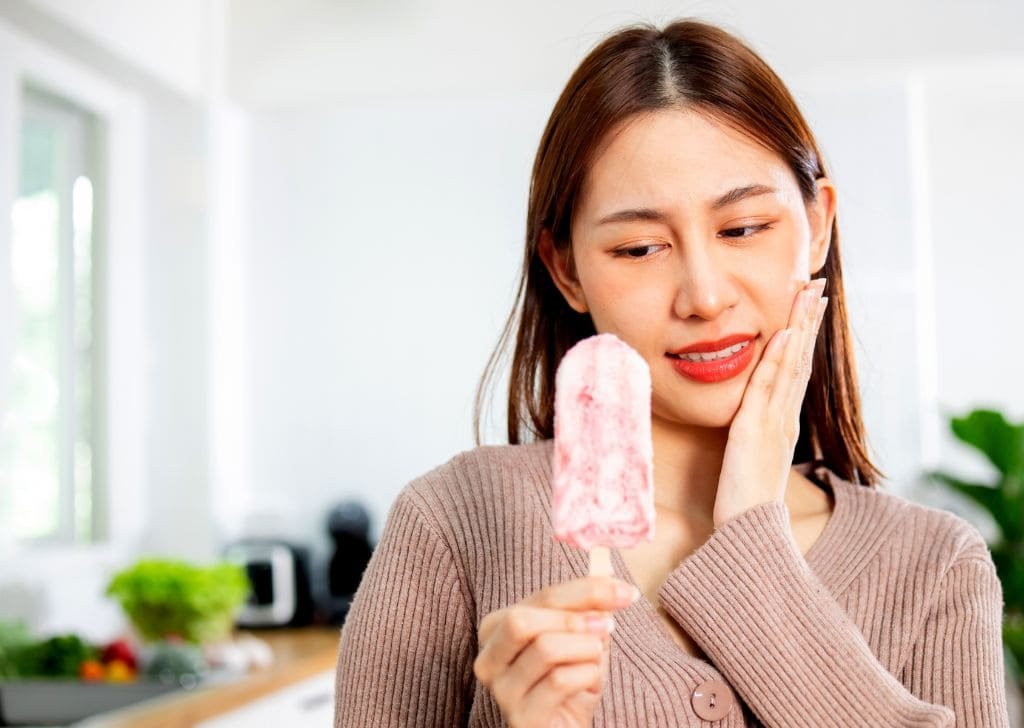 Woman experiencing tooth pain when eating an ice cream.