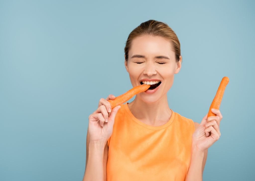 A woman eating crunch carrots and vegetables to whiten her teeth naturally.