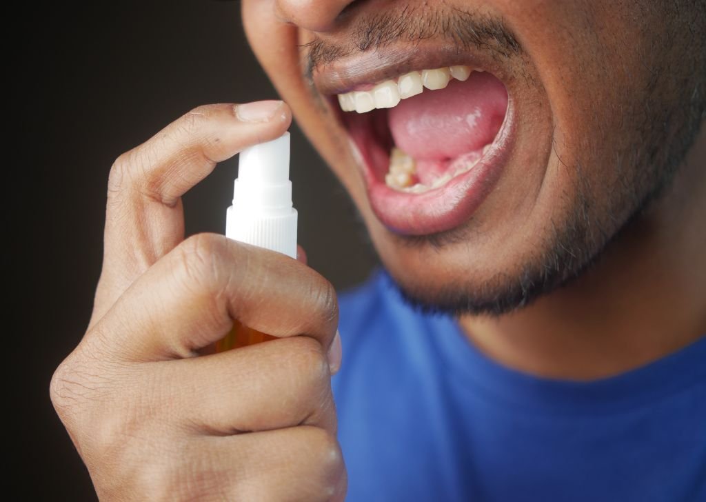 Man spraying mouth freshener with open mouth showing teeth and gums.