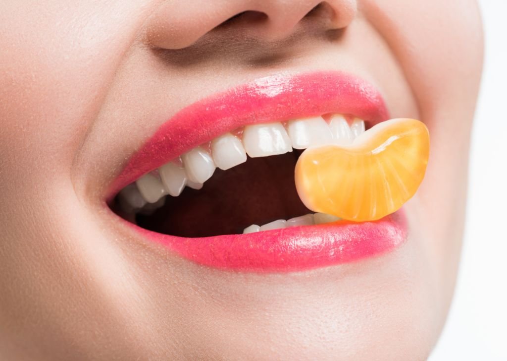 Healthy gums and teeth with an orange held between lips and teeth.