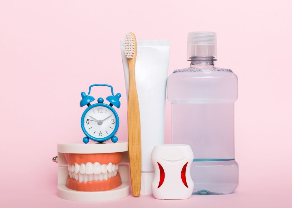 Dental hygiene tools including toothbrush, toothpaste, mouthwash, floss, and dentures with gums on pink background.